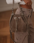 Sac seau taupe Fango en daim à franges et liens coulissants, porté à l’avant-bras