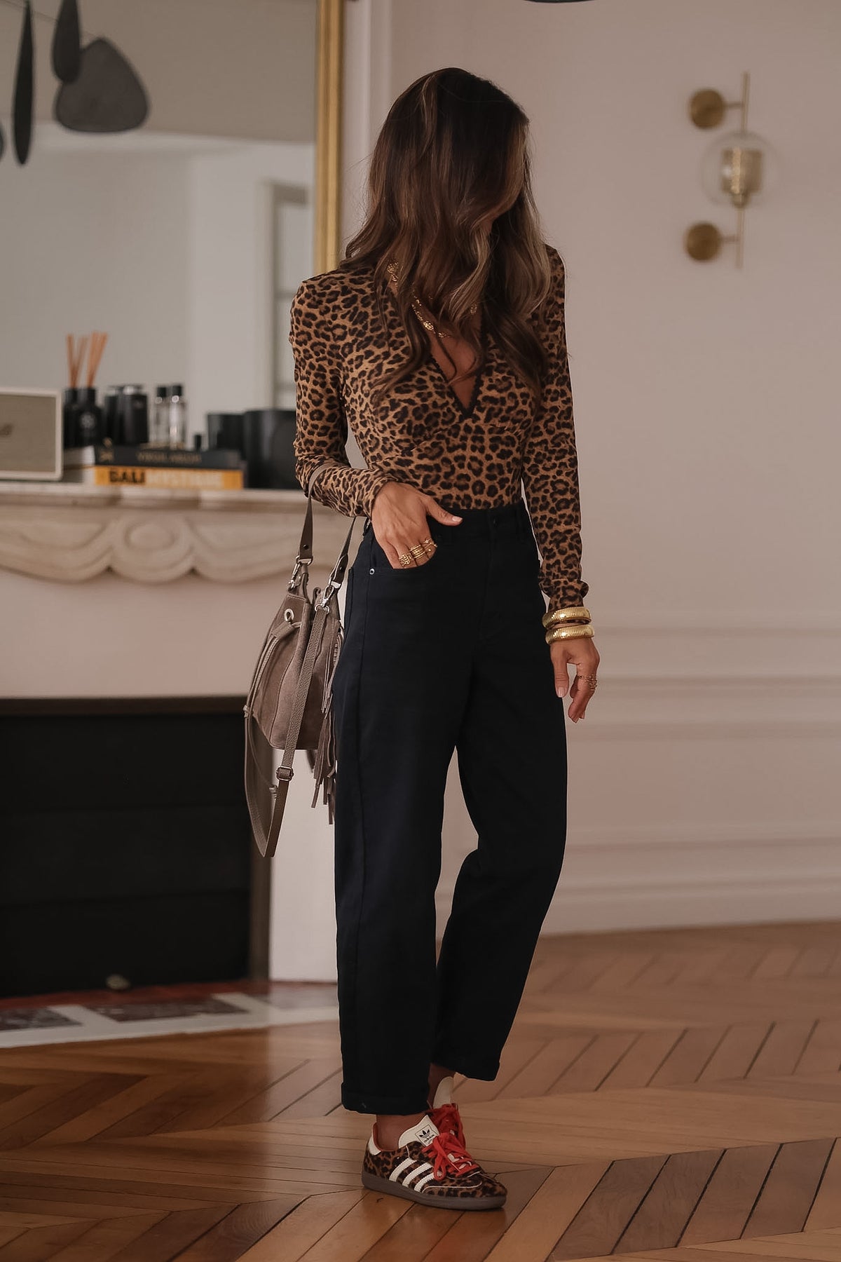 Jean noir Octave à coupe mom, porté debout jambes croisées avec un body léopard et un sac taupe