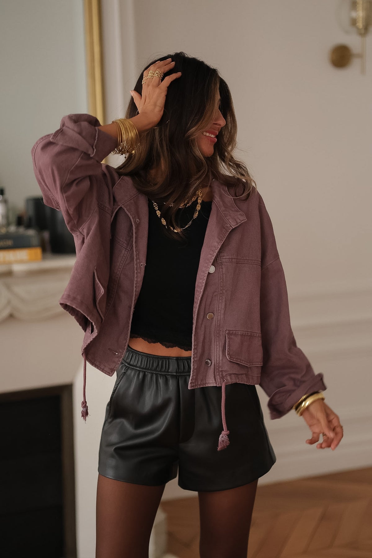 Veste en jean prune Suki à pressions argentées, portée ouverte avec un short noir, une main dans les cheveux