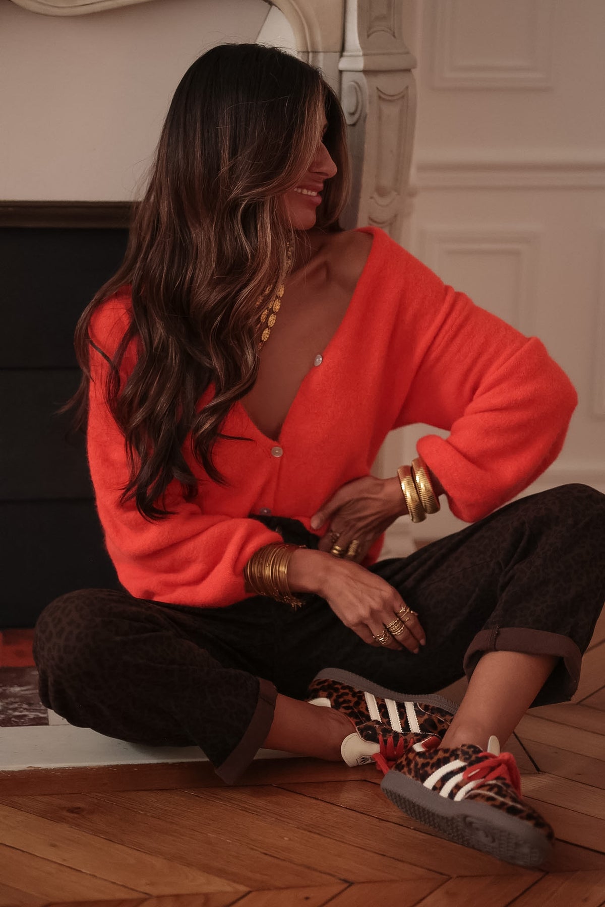 Gilet orange Harlow à col V et boutons, porté assise jambes croisées avec un jean léopard