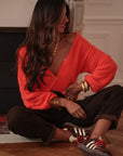 Gilet orange Harlow à col V et boutons, porté assise jambes croisées avec un jean léopard
