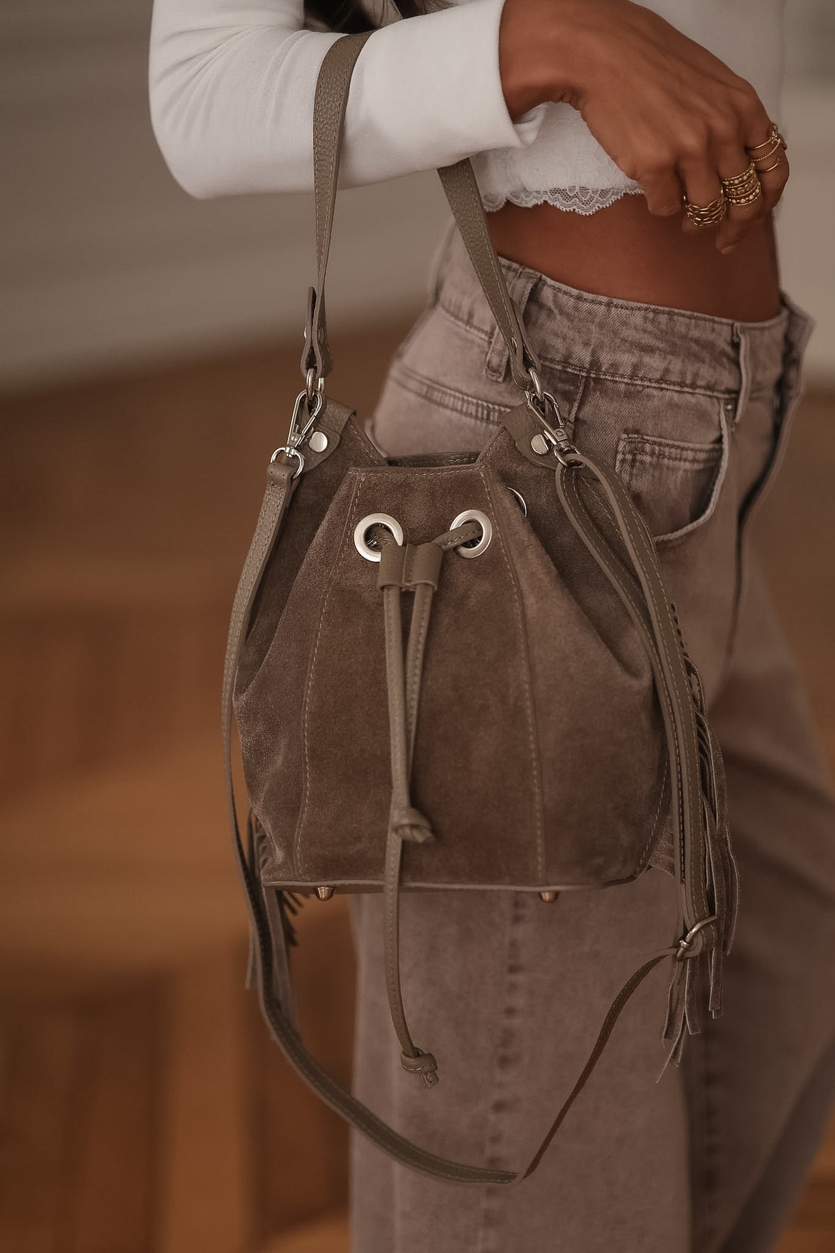 Sac seau taupe Fango en daim à franges et liens coulissants, porté à l’avant-bras